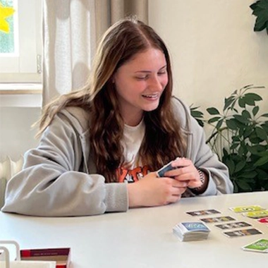 Eine junge Frau spielt Karten und schaut auf den Tisch. 