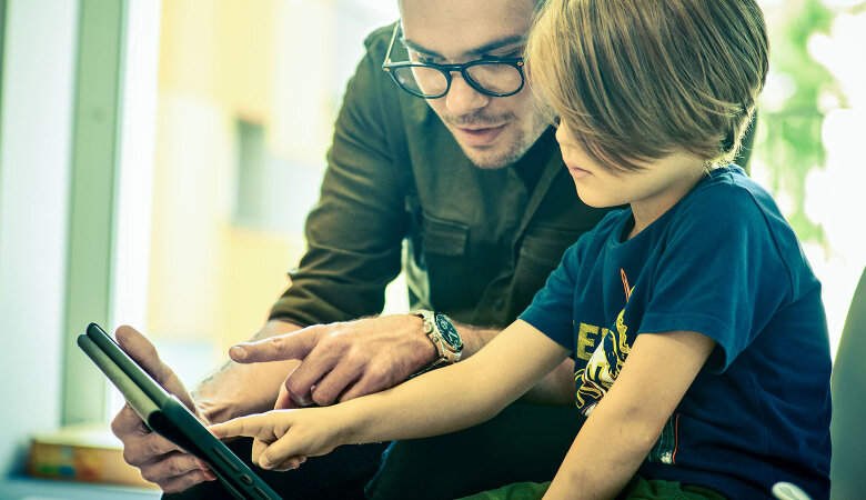 Szene im Kindergarten: Ein Erzieher und ein Junge bedienen zusammen ein Tablet.